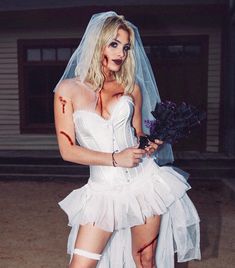 a woman dressed up as a bride with blood on her face and body, holding a bouquet of flowers