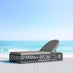 a lounge chair sitting on top of a wooden floor next to the ocean and sky