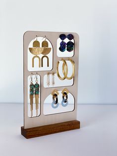 a wooden stand with earrings and earring holders on it's sides, in front of a white background