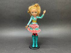 a doll with blonde hair and blue boots is standing on a black base holding her hand out