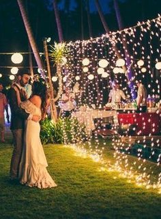 a couple standing next to each other on top of a lush green field covered in lights