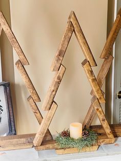 two wooden christmas trees sitting on top of a mantle next to a candle and some pine cones