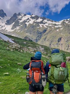 two people with backpacks are walking up a path in front of snow capped mountains