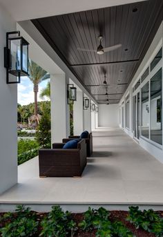 an outdoor covered porch with chairs and lamps on the ceiling, surrounded by greenery