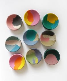 nine painted bowls sitting on top of a white table next to an orange, yellow, blue and pink one