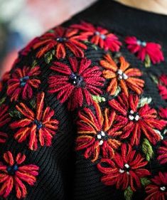 a woman wearing a black sweater with red and green flowers on it