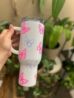 a hand holding a white coffee cup with pink and blue butterfly decals on it