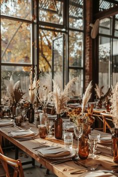 the table is set with place settings and vases filled with dried flowers, wheat stalks, and candlesticks