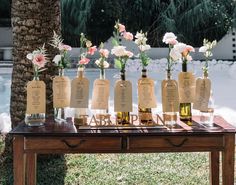 there are many bottles with flowers in them sitting on a wooden table next to a palm tree