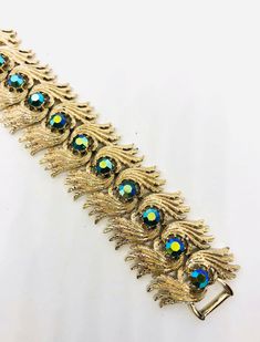 Fabulous vintage signed Coro Pegasus wide rhinestone bracelet. Beautiful blue AB rhinestones set in gold tone/plated textured modernist metal setting. In excellent vintage condition with minimal age appropriate wear.... if any. Doesn't appear to have been worn. Has secure fold over clasp. Stones securely set. Measures 1 3/8 inches wide 7 inches long.   Thanks for looking. Vintage Gold Bracelets With Sparkling Details, Vintage Gold Bracelets With Bling, Retro Jeweled Gold Jewelry, Vintage Gold Bling Bracelets, Retro Gold Jeweled Jewelry, Faux Fur Handbag, Interchangeable Earrings, Sterling Silver Owl, Vintage Designer Jewelry