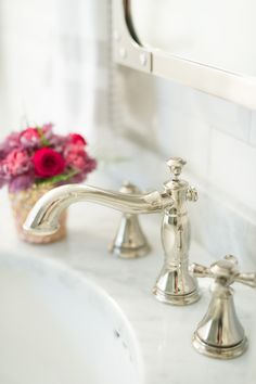 a bathroom sink with two faucets and a vase of flowers on the counter