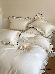 a white bed topped with pillows next to a candle