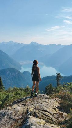 a woman standing on top of a mountain looking out at the mountains and lake below