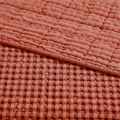 an orange quilted bed spread on top of a red blanket with checkered pattern