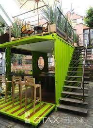 a green shipping container with stairs leading up to the second floor and an open balcony