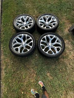 four rims and tires on the ground with someone's feet next to them