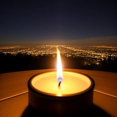 a lit candle sitting on top of a wooden table next to a night sky view