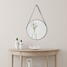 a round mirror hanging on the wall next to a table with vases and plants