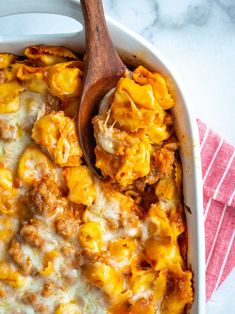 a casserole dish with meat and cheese in it on a pink towel next to a wooden spoon