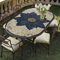 a mosaic table and chairs on the grass with flowers in vase sitting on top of it