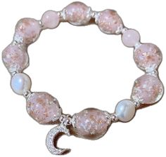 a pink bracelet with white beads and a crescent charm on the clasp, sitting in front of a white background