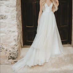 a woman standing in front of a door wearing a white dress and holding her hair back