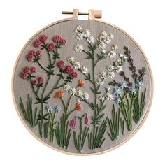 an embroidery pattern with flowers and grass on it's side, hanging from a wooden hoop