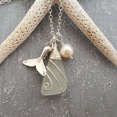 a close up of a necklace with a bird on it's back and pearls hanging from the side