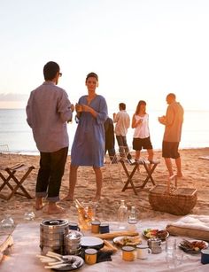 a group of people standing on top of a sandy beach next to the ocean in front of a picnic table