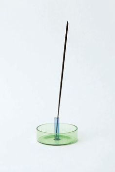 a green glass bowl with a black stick sticking out of the top, on a white background