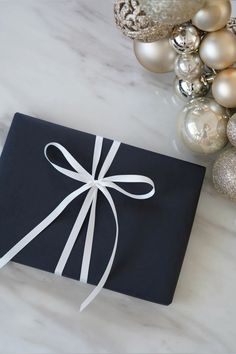 a black gift box wrapped in white ribbon with ornaments around it on a marble surface