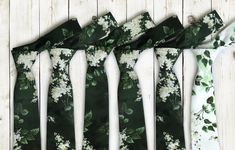 four ties with white flowers on them are lined up against a wooden wall, one is green and the other is white