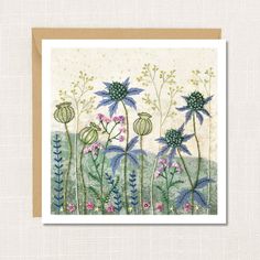 a greeting card with blue flowers and green leaves on the bottom, in front of a beige background