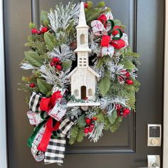 a wreath with a church on it hanging from the front door, decorated for christmas