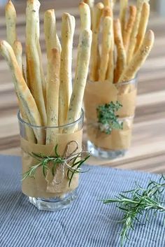 small glass vases filled with french fries on a blue table cloth next to a sprig of rosemary