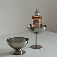 a bottle of gin in a silver bowl next to a metal cup on a white table