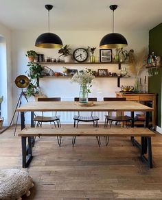 a dining room table and benches in front of a wall with hanging clocks on it