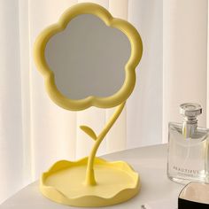 a yellow flower shaped mirror sitting on top of a table next to a bottle of perfume