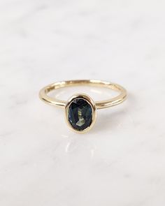 a gold ring with a blue stone in the center on a white marble countertop