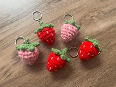 four crocheted strawberry keychains sitting on top of a wooden table