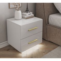 a white night stand with two drawers and a gold handle on the bottom, next to a bed