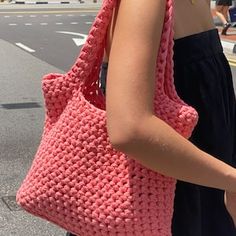 a woman carrying a pink crocheted handbag on the side of the road