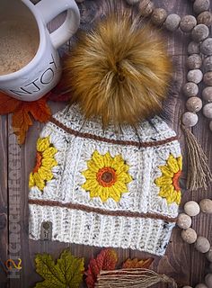 a knitted hat with sunflowers on it next to a cup of coffee