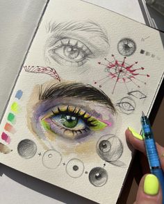 a person holding a pen and drawing on paper with colored pencils in front of them