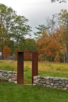 two tall metal sculptures in the middle of a grassy field with trees and grass behind them