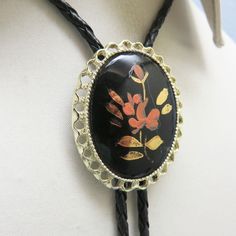 This lovely antique porcelain  bolo is made from a hand painted  cabochon.  It is a  floral scene on black porcelain.  It is very striking.   The bolo slide measures 2  inches tall and 1 5/8th inches wide. It is placed on a new 36 inch long braided black leatherette string tie with bright golden brass end caps. This fellow will arrive in a lovely gift box for easy gift giving.. If you like vintage bolo ties, western accessories, vintage Mexican and Native American silver and vintage jewelry, kin Vintage Black Ceremonial Jewelry, Vintage Black Bolo Ties For Gift, Vintage Black Bolo Ties As Gift, Artistic Black Collectible Jewelry, Artistic Black Enamel Jewelry, Vintage Black Hand-painted Jewelry, Vintage Black Hand Painted Jewelry, Black Porcelain, Western Accessories