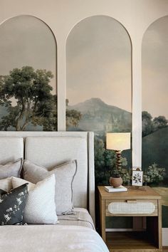 a bed sitting under two arched windows next to a table with a lamp on it