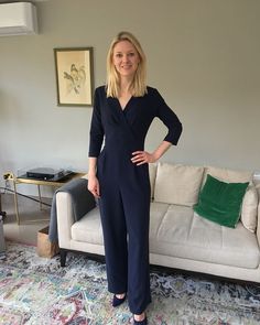 a woman standing in front of a couch wearing a navy blue jumpsuit and heels