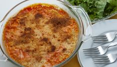 a casserole dish on a table with silverware and salad in the background