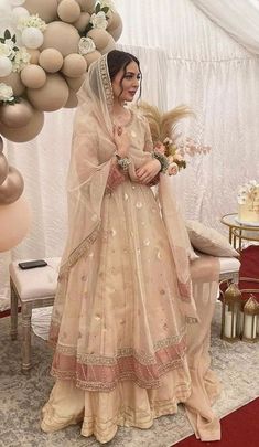 a woman in a wedding dress standing next to a balloon arch with flowers on it